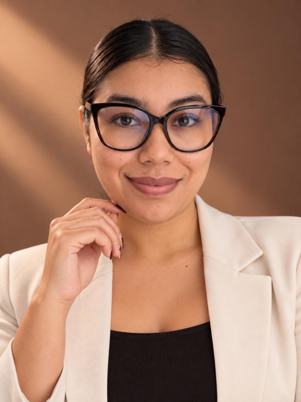 Retrato de Daniela Villafuerte Mena: sonríe, usa gafas y blazer claro sobre un fondo cálido